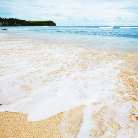 Mural de playa de arena en Bali con olas espumosas
